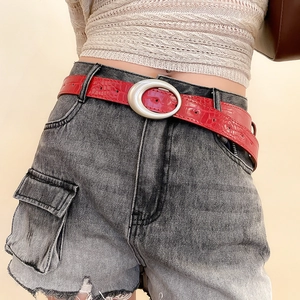 Detail view of red faux crocodile leather belt with silver oval buckle on denim shorts