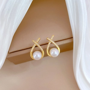 Detail of luxury gold earrings with crisscross crystal pavé and white hanging pearls