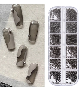 Macro shot of silver metal nail art beads in 12-grid box with marble manicure detail