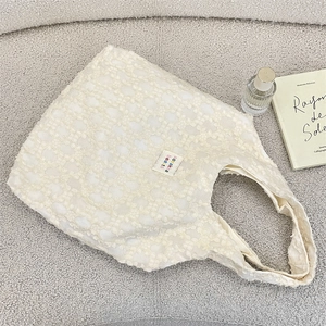 Close-up of cream textured floral jacquard tote bag with stylish label on gray fabric
