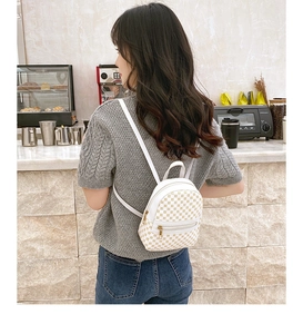 Back view of a mini white printed backpack worn by a model in a cozy cafe setting