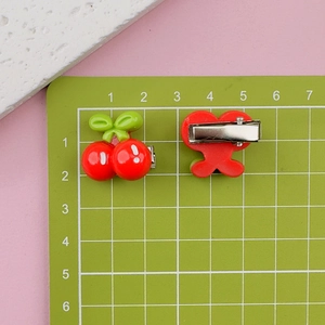 Detail view of red cherry hair clips with green leaves and silver metal BB clip base