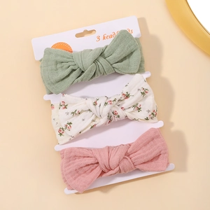 Detailed view of three knotted fabric baby headbands in green, floral and pink on display card
