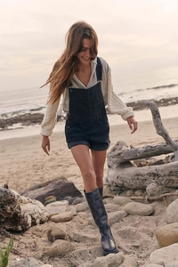 Outdoor shot of loose dark grey denim overalls styled with beige sweater and black boots