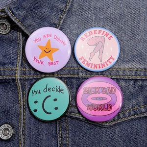 Close-up of four colorful round pins with illustrations on a blue denim jacket