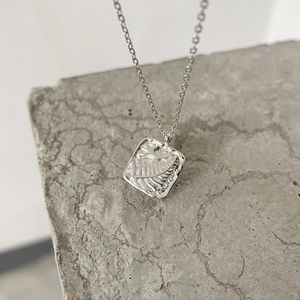 Macro shot of silver square pendant with hammered texture on a textured stone surface