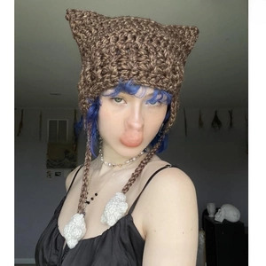 Detail of hand-knitted brown cat ear hat with punk style crochet strings and pom-poms