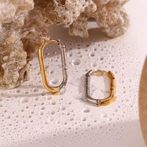 Detail of oval two-tone earrings in gold and silver finish resting on water droplets