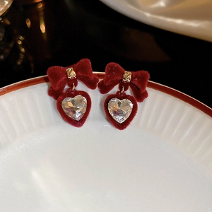 Gros plan boucles d'oreilles nœud velours rouge avec pendentif cœur cristal sur porcelaine