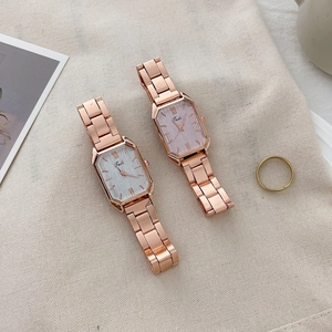 Detail view of rectangular quartz watches with rose gold metal bands on textured beige canvas