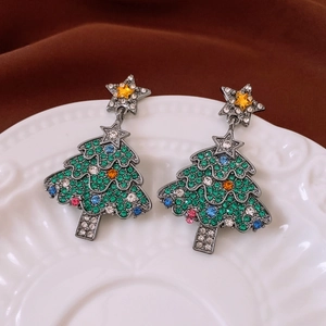 Detail view of silver needle Christmas tree earrings with colorful rhinestones on a plate