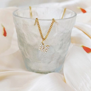 Macro detail of gold-plated letter M pendant with inlaid white pearls on a link chain