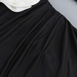 Detail of off-shoulder dress with black and white floral trim and silky pleated fabric texture