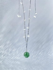 Détail du pendentif en pierre verte enveloppé de fil d'argent sur un cordon tressé gris