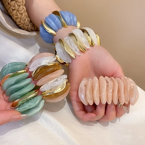 Detail view of wavy acrylic bangle bracelets with golden metal accents in various colors