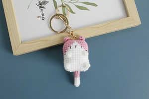 Close-up of handmade pink and white crochet cat keychain with metallic ring