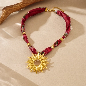 Detail of golden sun pendant with red floral silk ribbon chain on a natural sand background