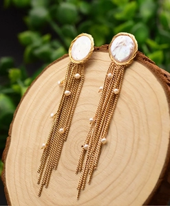Detailed view of baroque pearl gold tassel earrings placed on a natural wood slice