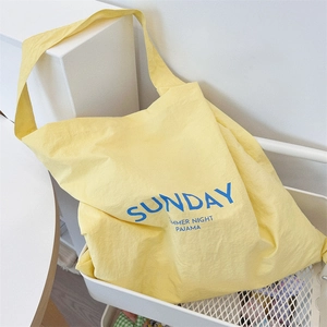 Detail of yellow canvas tote bag featuring blue Sunday letter print in a white wire basket