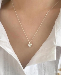 Close-up of a silver heart-shaped pendant necklace worn with a white striped shirt