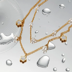 Macro detail of gold necklace with white pearl and shell flower pendant on water surface