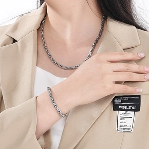 Detail shot of a silver chunky cable chain necklace and bracelet worn with a beige suit