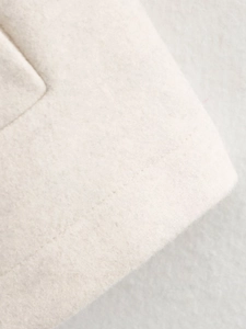 Macro shot of off-white wool blend fabric texture with fine stitching on coat edge