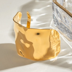 Close-up of golden wide open cuff bracelet featuring irregular hammered texture and modern style