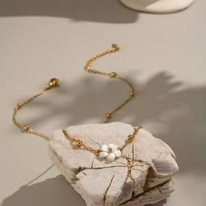 Gold stainless steel necklace featuring a white shell flower pendant on a natural stone