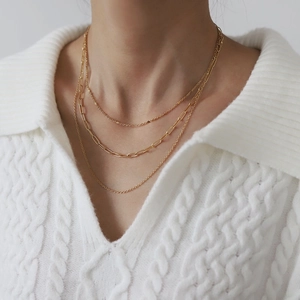 Close-up of layered golden stainless steel necklaces with paperclip links on knitwear