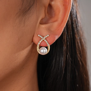 Detailed close-up of a gold X-shaped earring with small diamonds and a white pearl drop