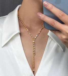 Détail d'un collier en Y doré avec zircons rectangulaires sur chemise en satin