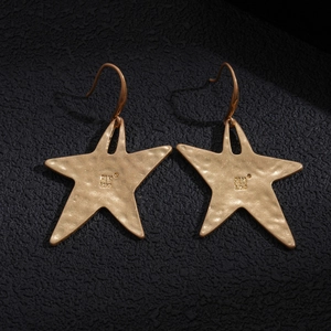 Minimalist gold star earrings with hammered texture on a sleek black background