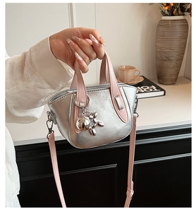 Détail d'un sac argenté avec poignées roses et breloque en forme de chien ballon