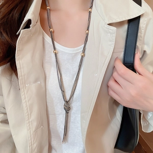 Close-up of a layered chain tassel necklace with golden beads on a beige trench coat