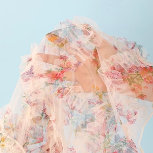Detail view of sheer pink floral mesh fabric with elegant ruffled edges and vibrant flower prints