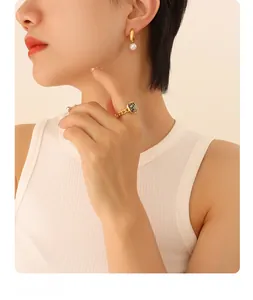 Detail of gold pearl earrings and a dalmatian stone chain ring worn by a model