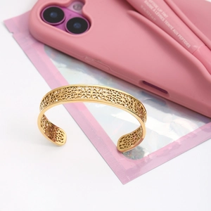 Détail d'un bracelet doré à motif dentelle ajouré posé sur un fond rose élégant