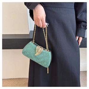Detail of dark green textured clutch bag with gold leaf clasp and delicate chain strap