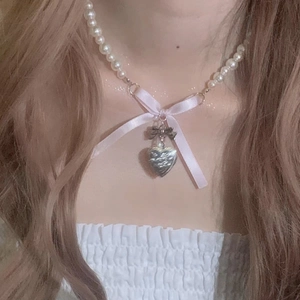 Close-up of pearl necklace with pink ribbon bow and silver heart pendant on neck