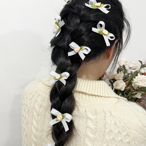Détail de barrettes nœuds blancs avec rose rose et feuilles vertes sur cheveux tressés