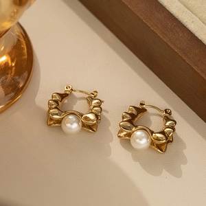 Elegant gold wave hoop earrings with large round pearls on a textured background