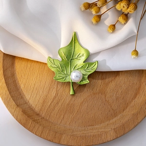 Detail view of a green maple leaf brooch with a white pearl on a wooden tray