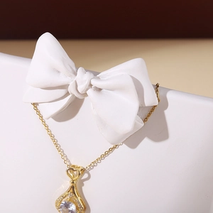 Gold necklace with heart pendant on white bow stand with minimalist light and shadow