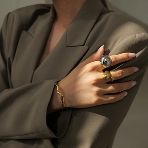 Polished 18K gold wave bangle and chunky rings set styled on a model in beige blazer