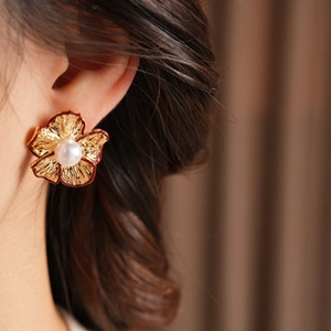 Nahaufnahme der goldenen Blumenohrringe mit Perle auf dem Ohr des Models