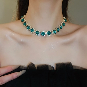 Close-up of a gold-tone necklace featuring green gemstone floral pendant on a model's neck