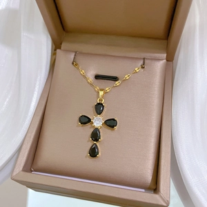 Macro view of gold cross necklace with black teardrop stones in a luxury gift box