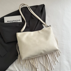 Retro cream white large crossbody bag with tassel and rivets on a blazer and book background