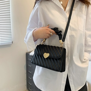 Fashionable black pleated handbag with wave quilting and golden heart lock on a model